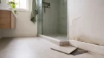 Modern bathroom showing peeling paint, mould and a loose floor tile caused by waterproofing failure.